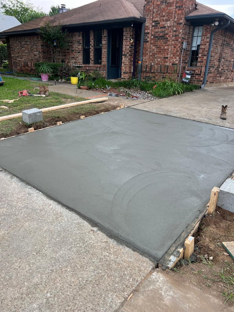 Concrete driveway under construction in front of a brick single-story house with landscaping and potted plants